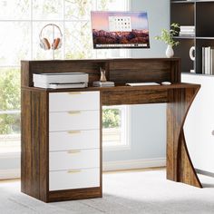 a desk with a computer monitor and headphones on it in front of a window