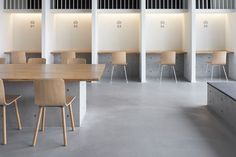 two people sitting at desks in a large room with white walls and wooden chairs