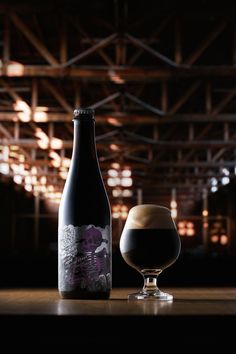 a bottle of beer next to a glass filled with dark liquid on a wooden table