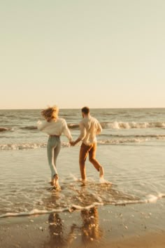 two people are running on the beach holding hands