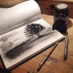 an open book on a wooden table next to a pen and ink pot with a tree drawn on it