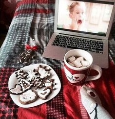 a laptop computer sitting on top of a bed next to cookies and marshmallows