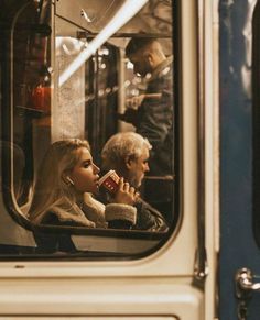 a woman sitting on a bus drinking from a cup while another man looks out the window