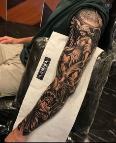 a man is sitting down with his arm covered in black and grey tattoos on it