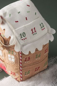 a gingerbread house made out of felt with numbers on the front and sides, sitting on top of a pile of white fluffy fabric