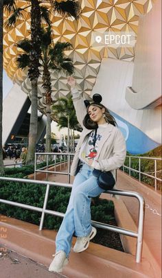 a woman sitting on top of a metal rail next to palm trees in front of a building