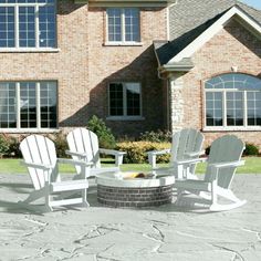 three chairs around a fire pit in front of a brick house