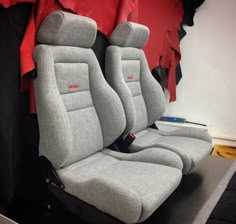 two gray seats sitting next to each other in front of a red shirt on display