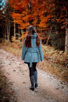 a woman walking down a dirt road in front of trees with orange leaves on it