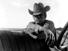 a man in a cowboy hat leaning on the steering wheel of a car with his hand resting on the driver's arm