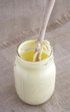 a jar filled with yellow liquid sitting on top of a tablecloth next to a spoon