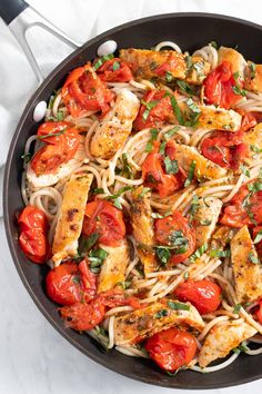 a skillet filled with chicken, tomatoes and pasta on top of a white table