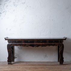 an old wooden table sitting on top of a hard wood floor next to a white wall