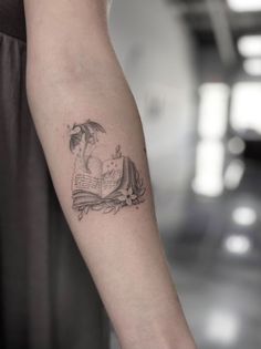 a woman's arm with a book and an umbrella tattoo on her left forearm