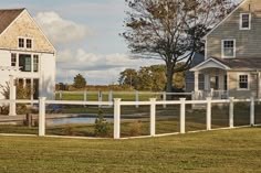 a white picket fence is in front of two houses with trees and grass on the other side