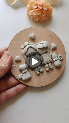 a hand holding a piece of art made out of clay and stone chips on top of a table