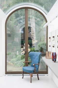 a blue chair sitting in front of a large window next to a plant filled wall