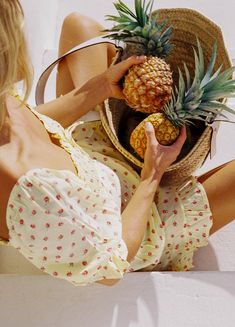 a woman sitting on the ground holding a basket with pineapples in her hands