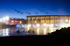 people are in the water at night near a large building with lights on it's sides