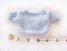 a blue knitted sweater next to a measuring tape on a white surface with the needle pointing towards it