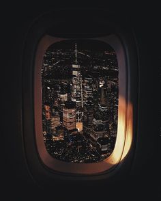 an airplane window showing the view of city lights and skyscrapers at night from above