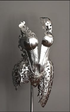 a metal sculpture with an intricate design on it's face and chest, in front of a gray wall