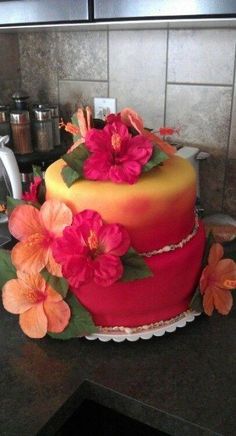 a red and yellow cake with pink flowers on the top is sitting on a counter