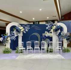 a blue and white wedding set up with flowers on the back wall, chairs in front of it