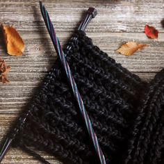 two knitting needles laying next to each other on top of a wooden table with leaves