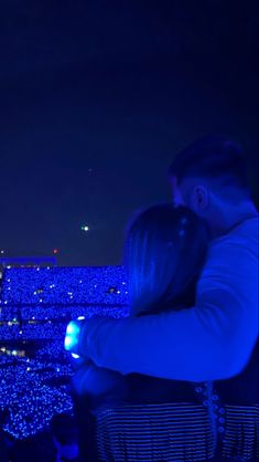 two people are looking at their cell phones in front of an audience with bright blue lights