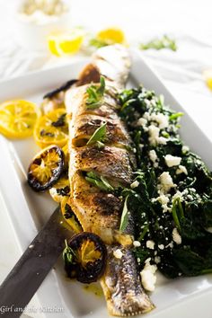 fish and vegetables on a white plate with a knife next to it, ready to be eaten