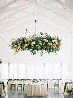 a room with tables and chairs covered in white linens, flowers hanging from the ceiling