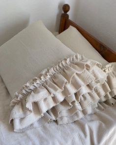 an unmade bed with white linens and ruffled pillows