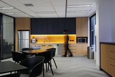 a man is walking through the kitchen in this modern office building with wood cabinets and black chairs