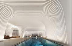 an indoor swimming pool surrounded by white walls and ceilinged with wavy lines on the ceiling