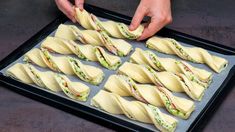 a tray filled with lots of sandwiches on top of a table next to a person's hand