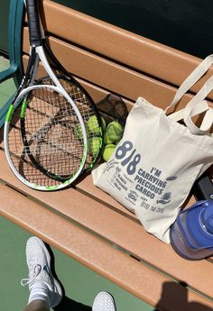 a tennis racket, ball and bag sitting on a bench next to a person's feet