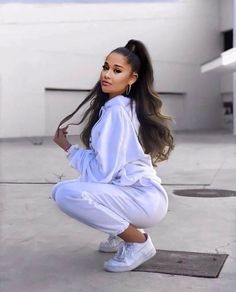 a woman kneeling down on the ground with her hair in ponytails and white sneakers