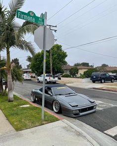 a car parked on the side of a street next to a stop sign and palm tree