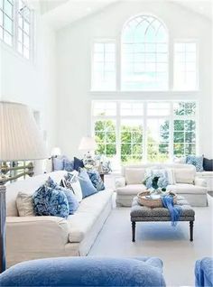 a living room with white furniture and blue pillows on the couches, in front of a large window