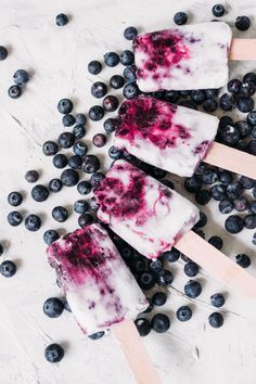 three popsicles with blueberries and ice cream on them, surrounded by fresh blueberries