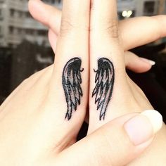 two black angel wings tattoo on both wrist and finger tattoos are shown in front of each other