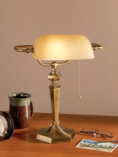 a desk lamp sitting on top of a wooden table next to a clock and glasses