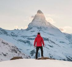 a man standing on top of a snow covered mountain looking at the mountains in the distance