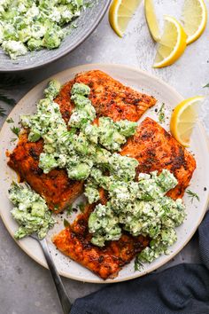 two plates filled with chicken covered in guacamole and garnished with lemon wedges