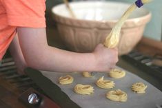 a person holding a spoon over some uncooked food on a baking sheet in front of a bowl