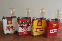 four old gas cans are lined up on a table with light bulbs in the top