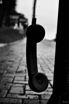 an old phone hanging from a pole on the side of a road in black and white