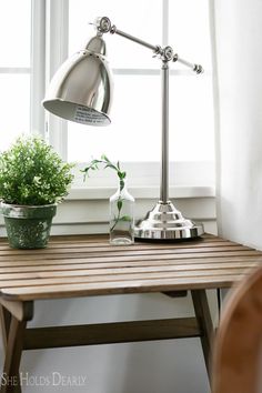 a desk with a potted plant on it and a lamp in front of the window