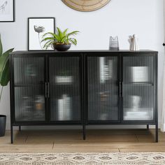 a black cabinet with glass doors and plants on top in front of a white wall